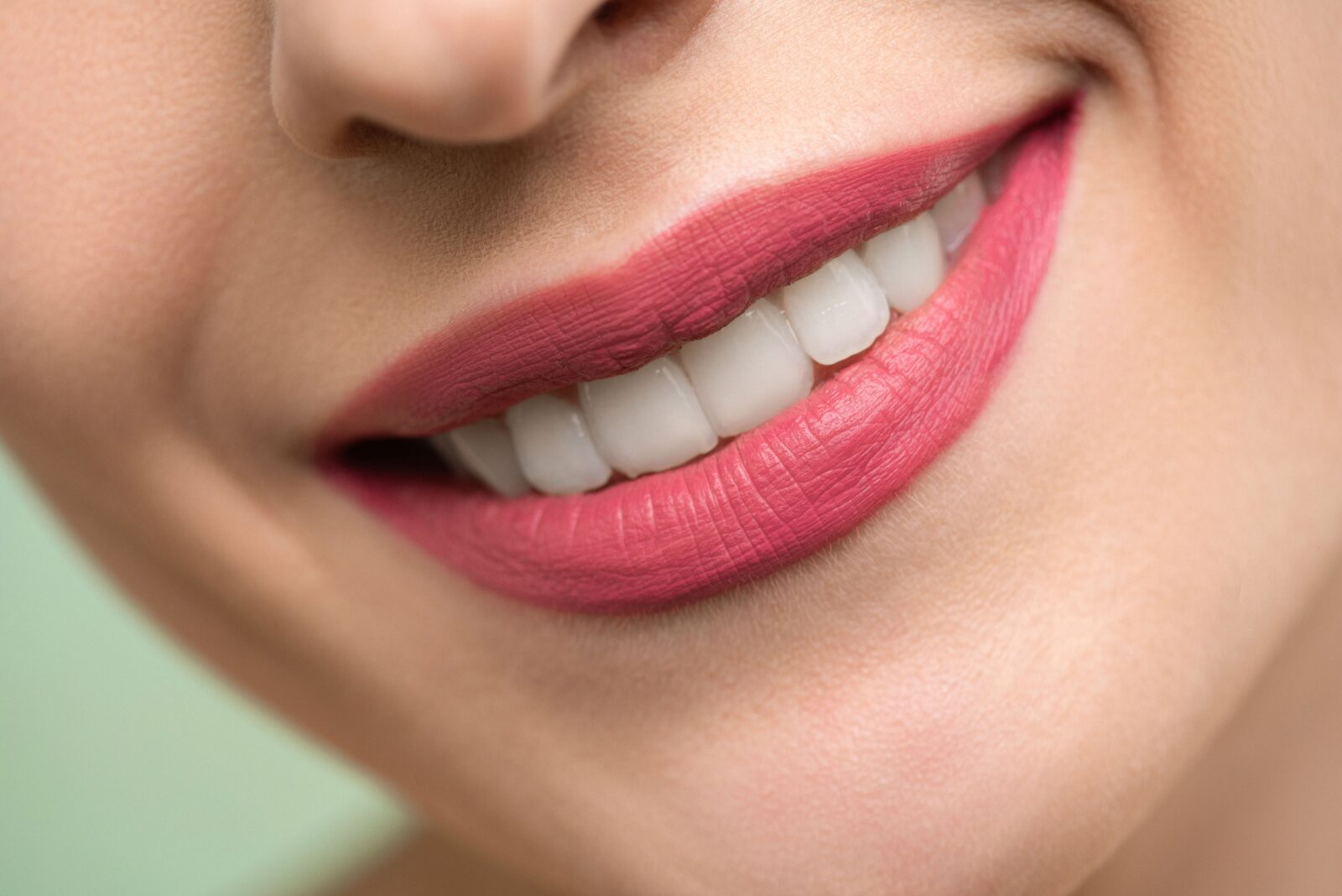 http://Vivid%20close-up%20image%20of%20a%20woman's%20smile%20showcasing%20red%20lipstick%20and%20white%20teeth%20on%20a%20light%20background.