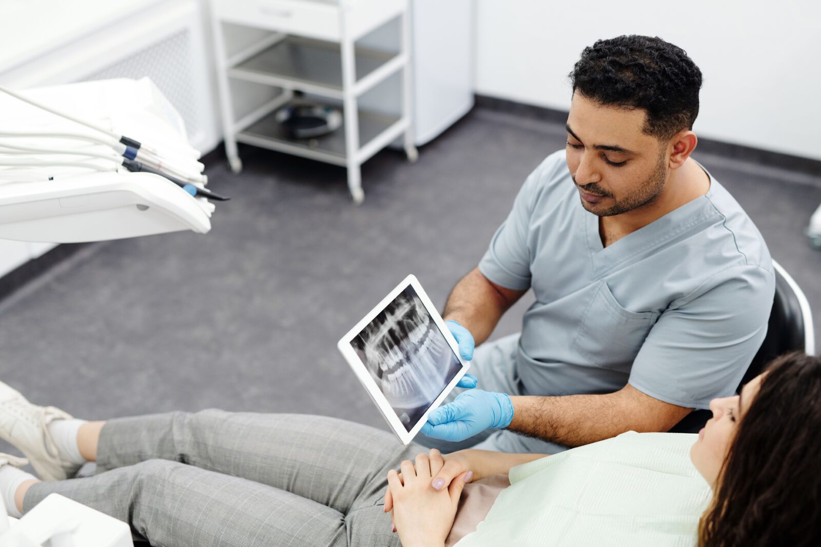 http://Dentist%20showing%20dental%20x-ray%20on%20tablet%20to%20a%20patient%20in%20modern%20clinic%20setting.